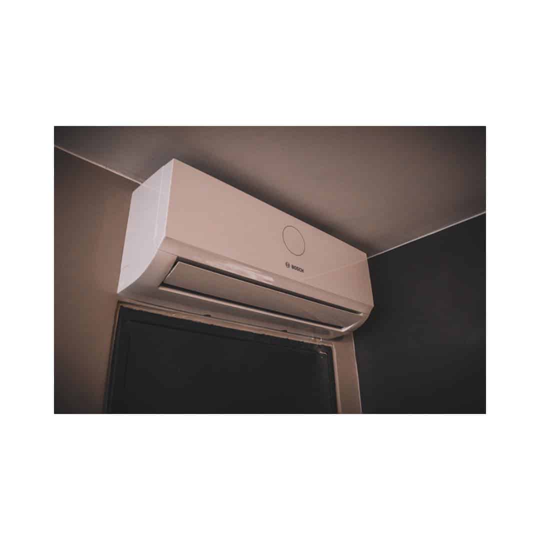 Climatiseur mural Bosch blanc installé sous un plafond, affichant un cercle de contrôle et le logo au centre.